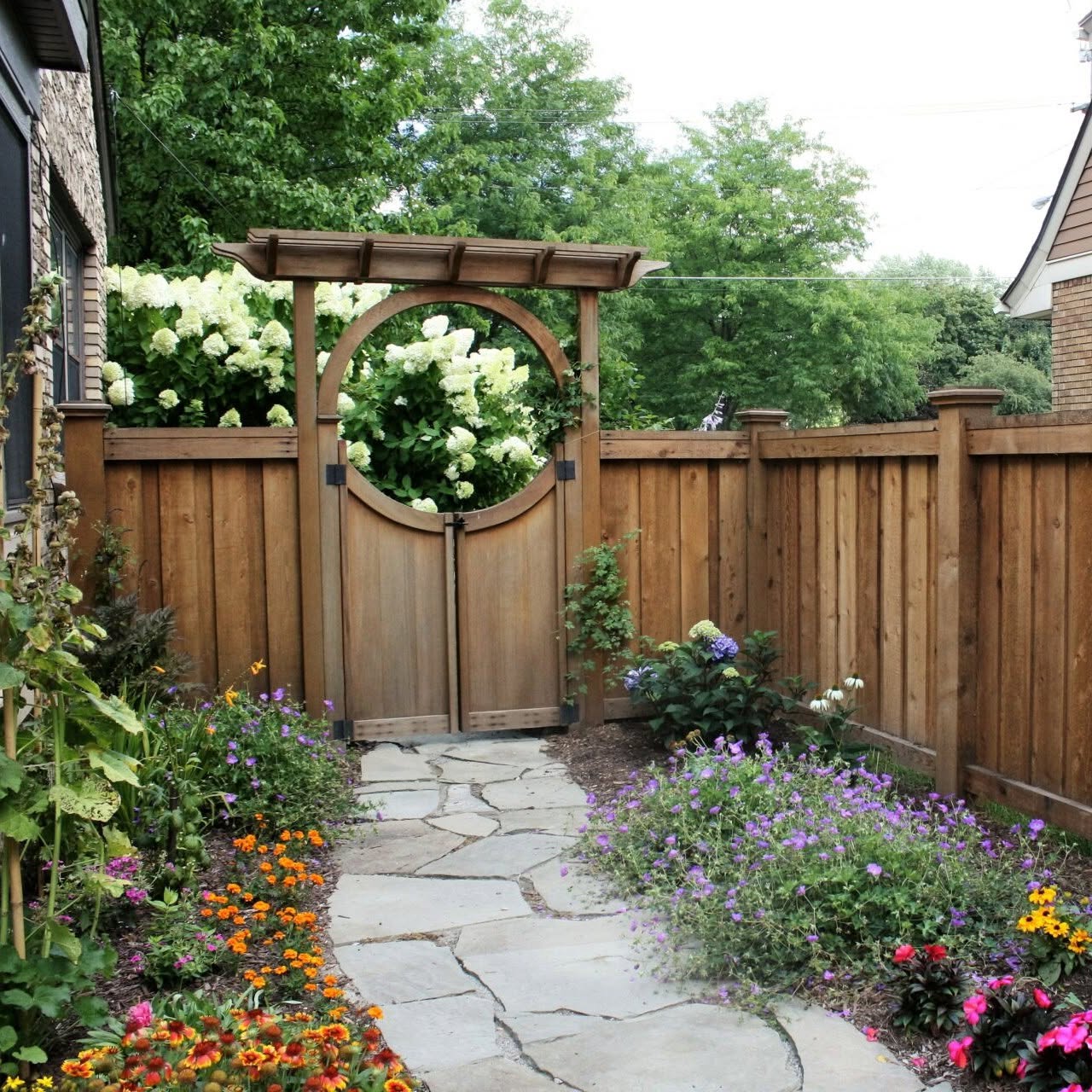 Custom cedar garden gate with a round window and arbor in a flower garden
